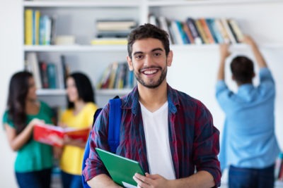 Laughing Spanish Male Student With Group Of Students At Library