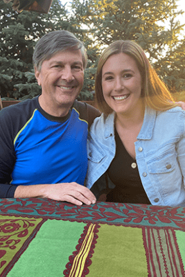 Photo of a white man with gray hair and a young woman smiling outdoors