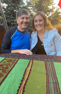 Photo of a white man with gray hair and a young woman smiling outdoors