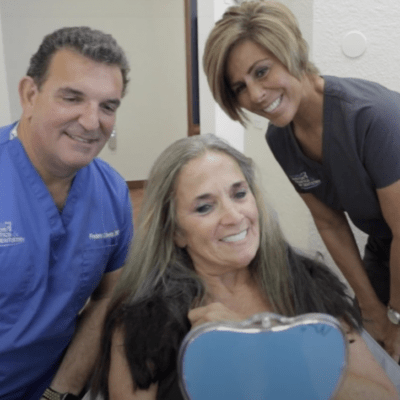 Female patient smiling because she was satisfied with her treatment next to 2 smiling dentists