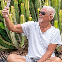 Handsome Middle-aged Man Takes A Selfie In Front Of A Large Cactus In An Exotic Seaside Resort